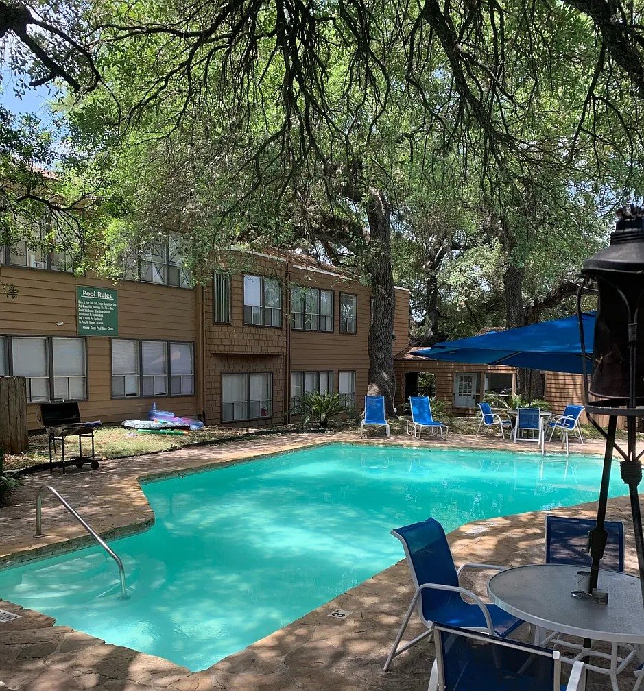 A pool surrounded by trees and chairs.
